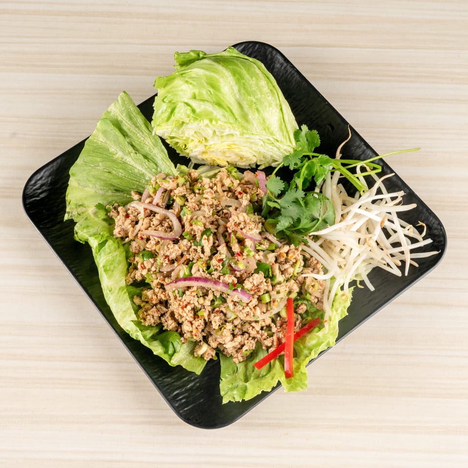 Minced meat salad (Larb) with lettuce, bean sprouts, cilantro, and red chili on a black plate.