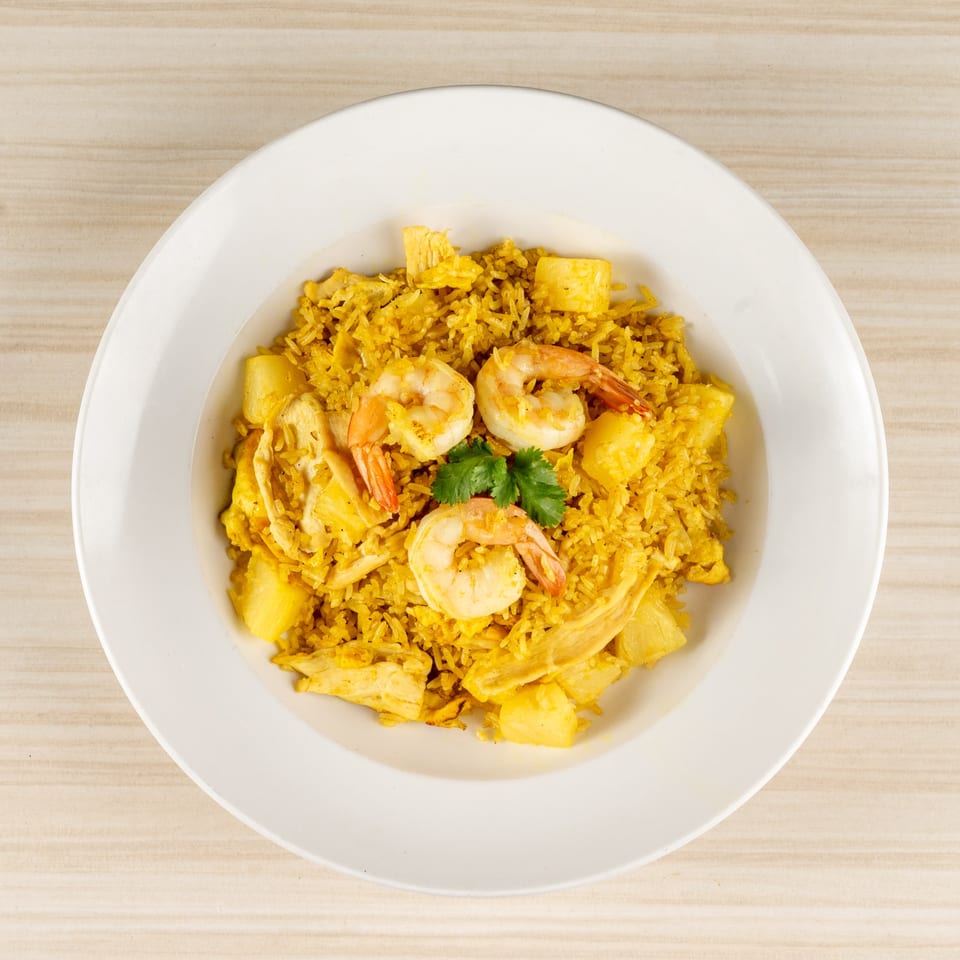 White plate of yellow fried rice with shrimp, chicken, pineapple, and cilantro garnish.