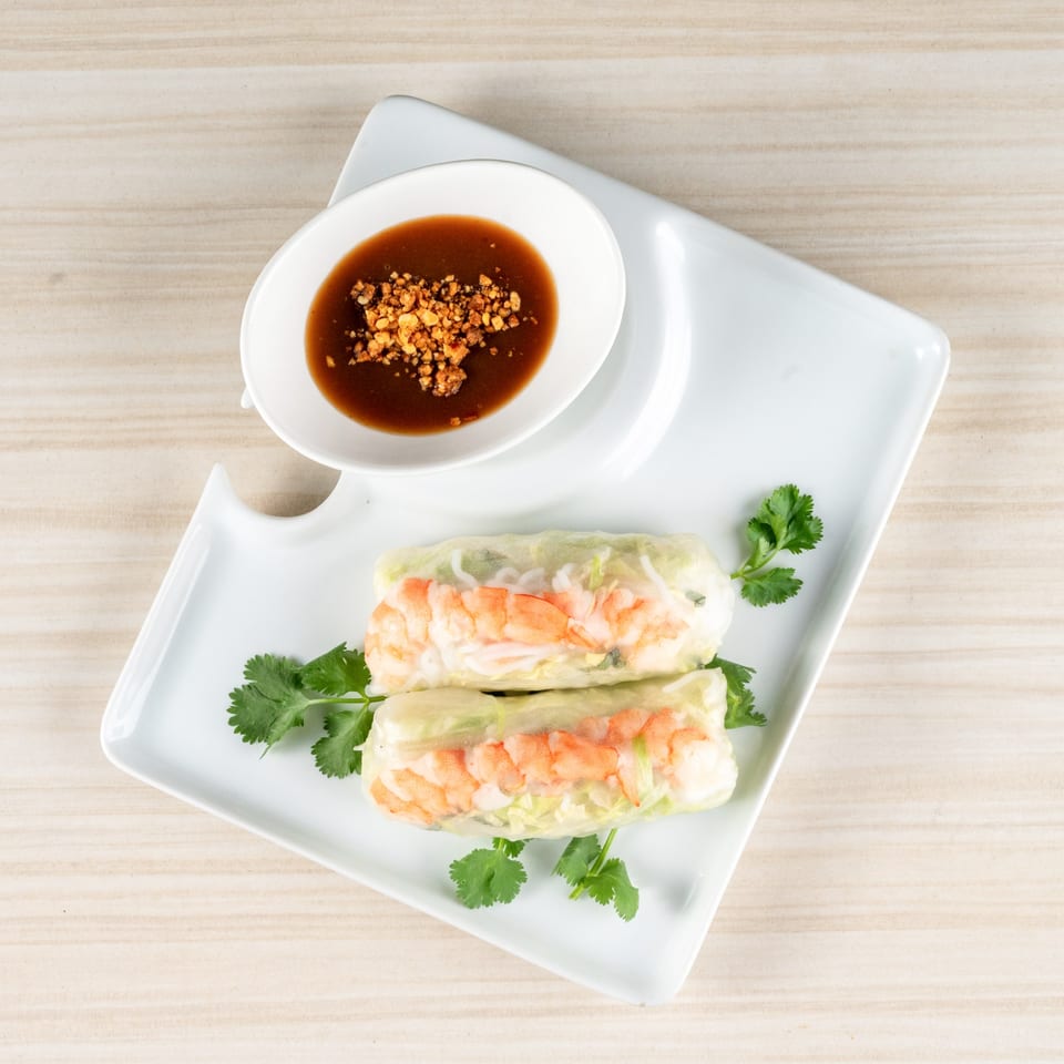 Two shrimp spring rolls with cilantro garnish and a side of peanut dipping sauce.
