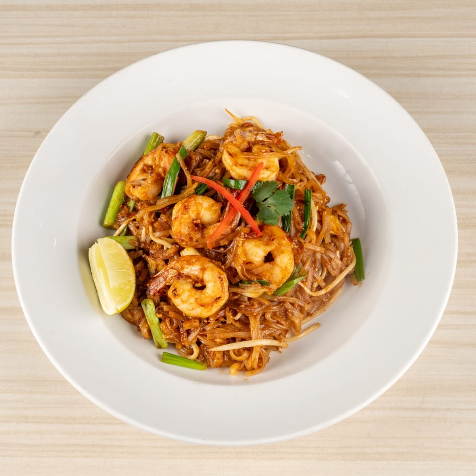 Shrimp Pad Thai with lime, green onions, and red chili on a white plate.