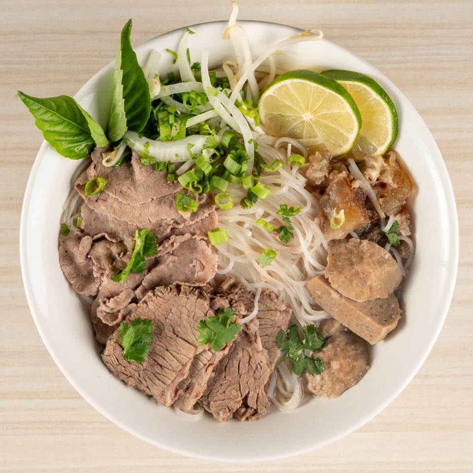Overhead view of a large bowl of pho with sliced beef, noodles, basil, lime, and fresh garnishes.