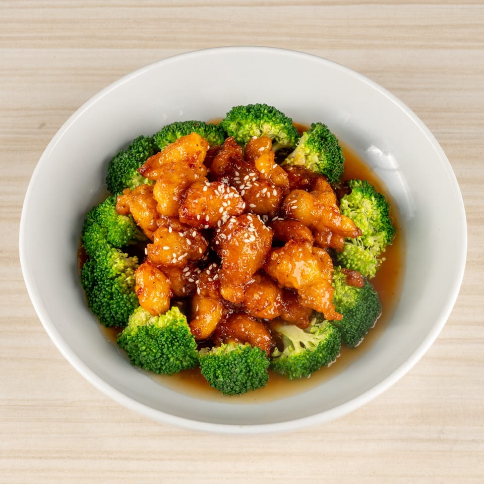 Orange chicken with broccoli and sesame seeds in a white bowl.